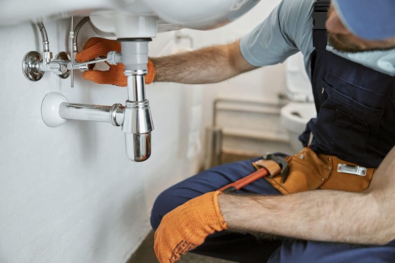 a plumber fixing signs of a plumbing problem by adjusting pipes under a sink